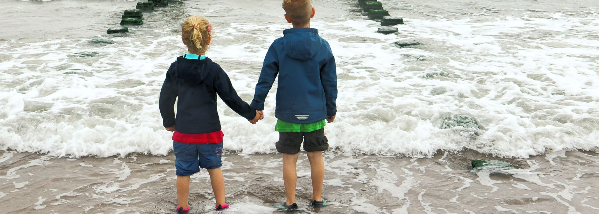Zwei Kinder gehen Hand in Hand am Meer entlang